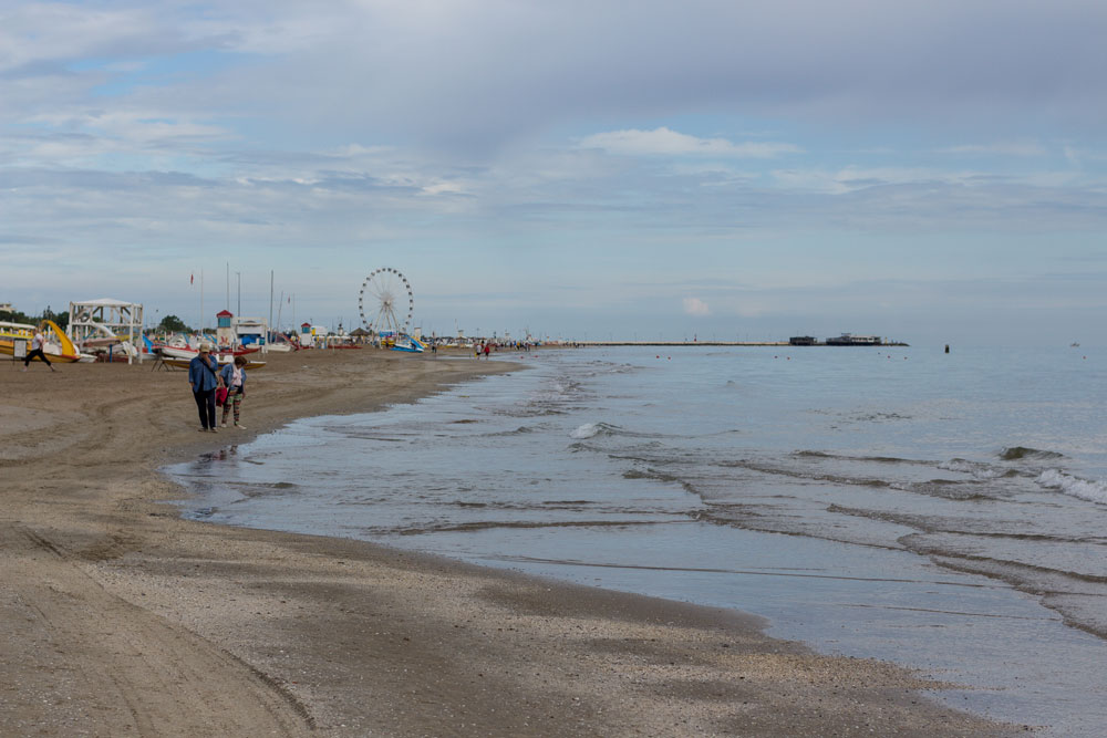 В начале пляжной линии прибрежная полоса кажется не такой уж и ухоженной. На заднем плане виднеется местное колесо обозрения Римини и причал.