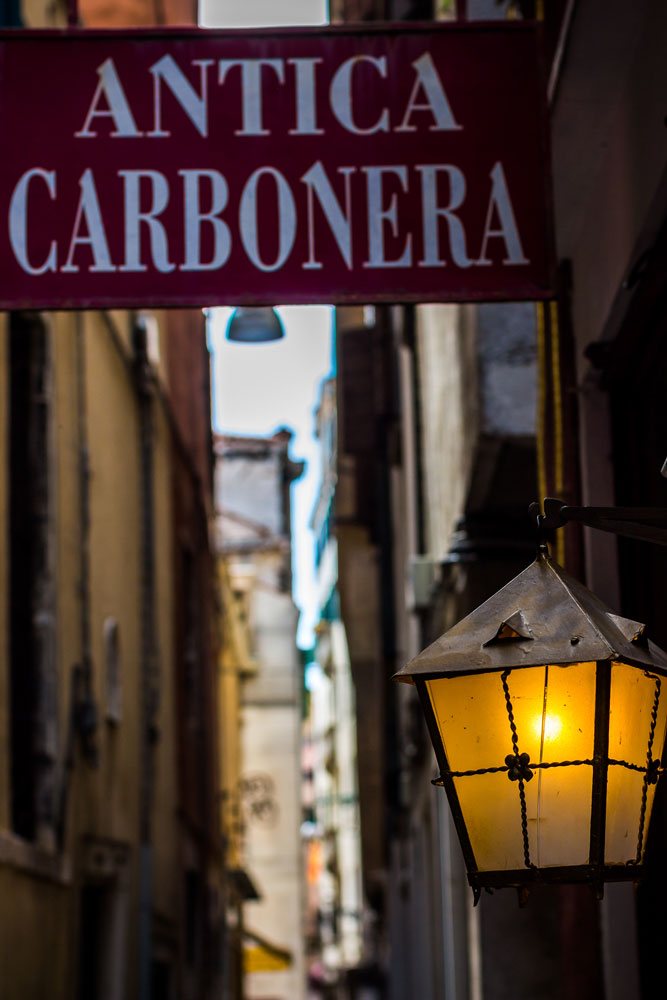 Фонарь на одной из улиц Венеции на фоне вывески заведения для туристов