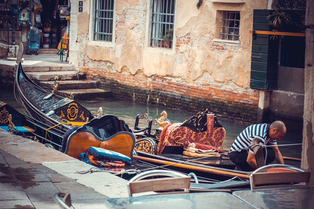 Гондольер в Венеции что-то поправляет на своей лодке