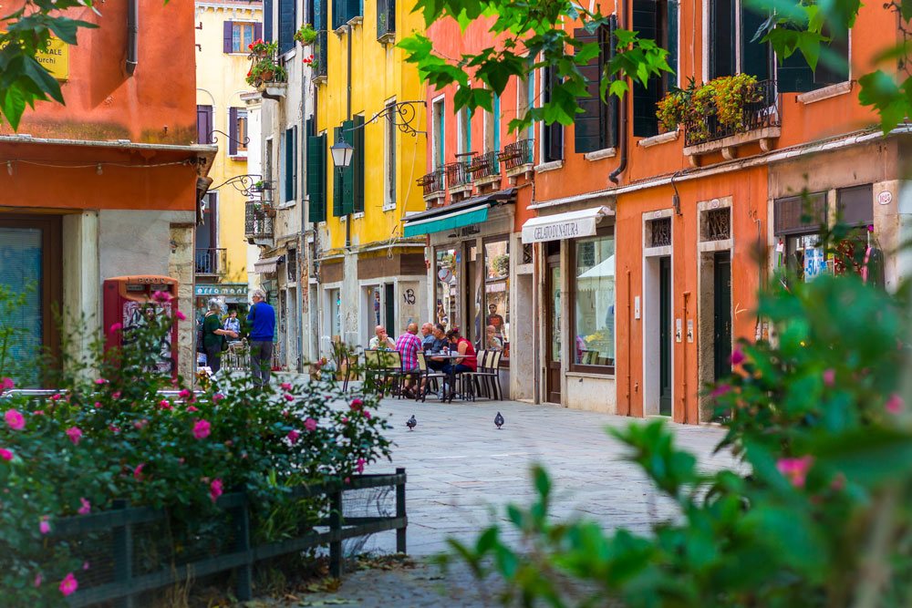 Пестрящие, разноцветные улицы и дома в Венеции на фоне цветов и зелени