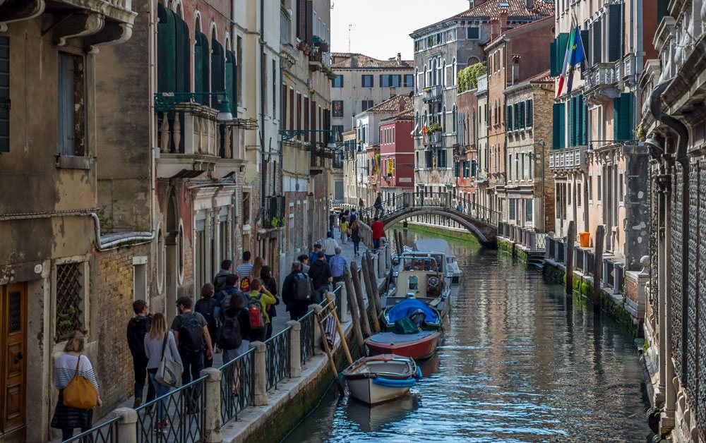 Небольшой канал в Венеции, толпа туристов и лодки у причала